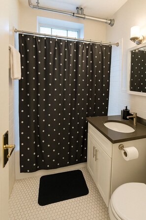A bathroom with a black and white polka dot shower curtain, a white sink with a black faucet, and a white toilet. - Hyde Park Trendy Studio Apartment in Good Spot (Chicago)