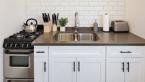 A modern kitchen with a stainless steel stove, double sink, and white cabinetry. - Hyde Park Trendy Studio Apartment in Good Spot (Chicago)