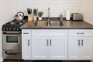 A modern kitchen with a stainless steel stove, double sink, and white cabinetry. - Hyde Park Trendy Studio Apartment in Good Spot (Chicago)