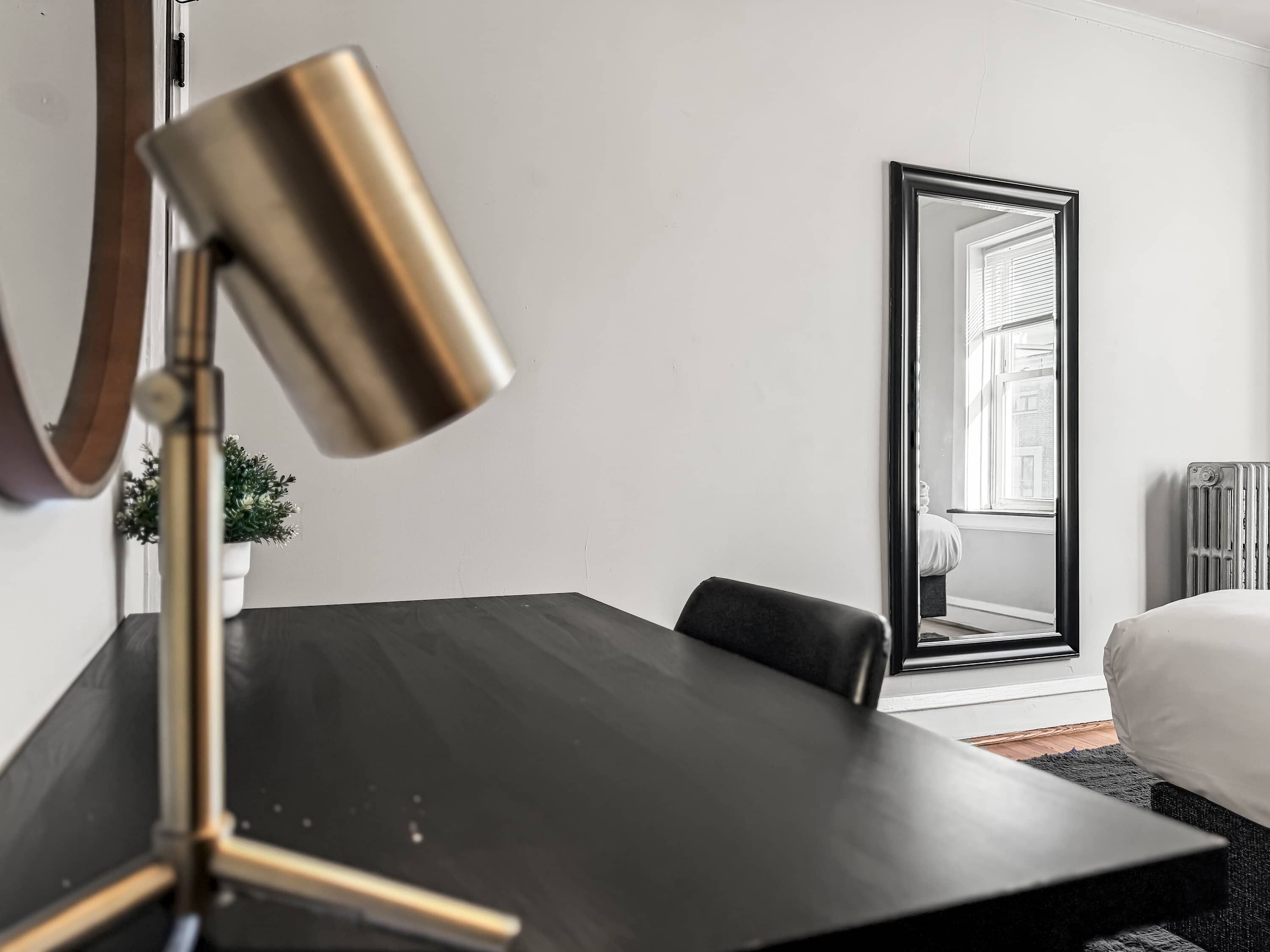 Una habitación de hotel moderna con un escritorio de madera oscura, una lámpara de pie dorada, un espejo grande y una planta en maceta.