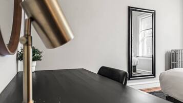 Una habitación de hotel moderna con un escritorio de madera oscura, una lámpara de pie dorada, un espejo grande y una planta en maceta.