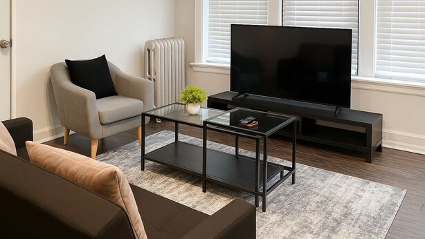 Moderni olohuone, jossa on sohva, nojatuoli, sohvapöytä, TV-taso ja patteri.