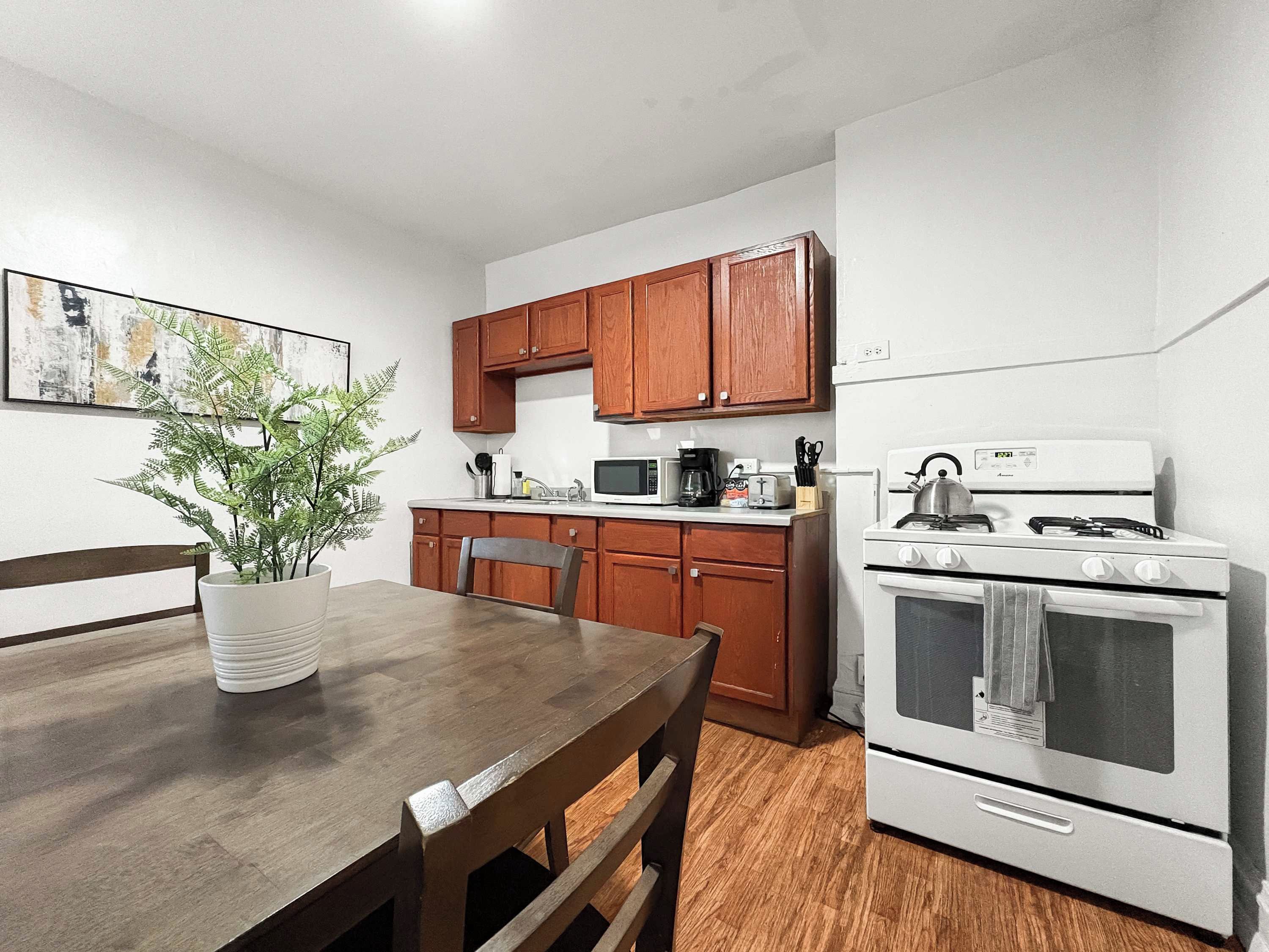 A compact kitchen with wooden cabinets, a microwave, a stove, and a dining table with chairs.
