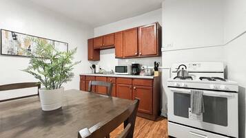 A compact kitchen with wooden cabinets, a microwave, a stove, and a dining table with chairs.