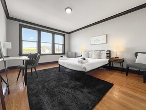 Una habitación de hotel moderna con una cama grande, un escritorio, una silla y vistas al exterior.