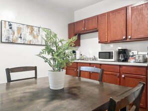 Una mesa de comedor con sillas, una planta en maceta, armarios de madera y un microondas en una cocina.