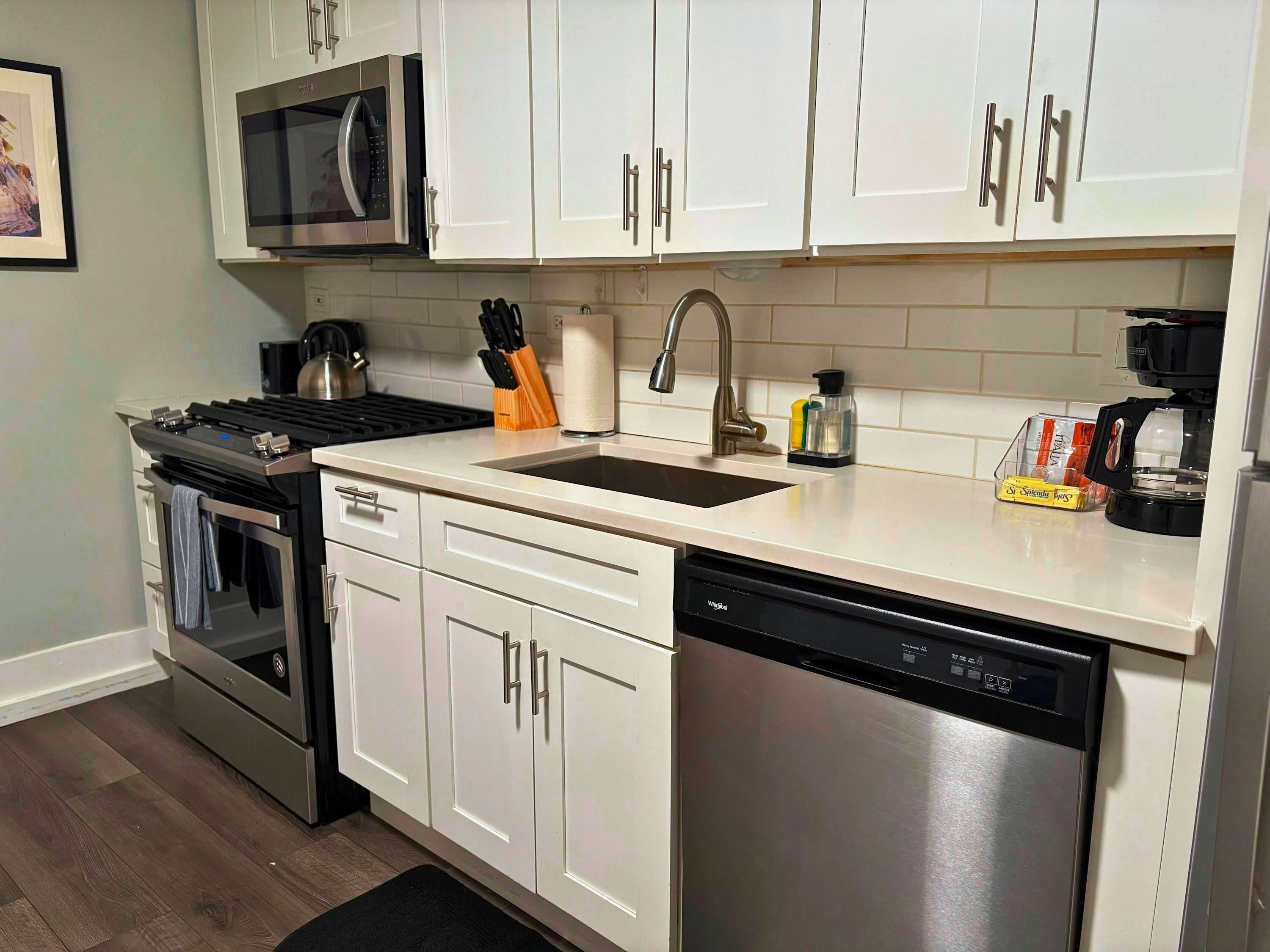 A modern kitchen with white cabinets, stainless steel appliances, and a black dishwasher.
