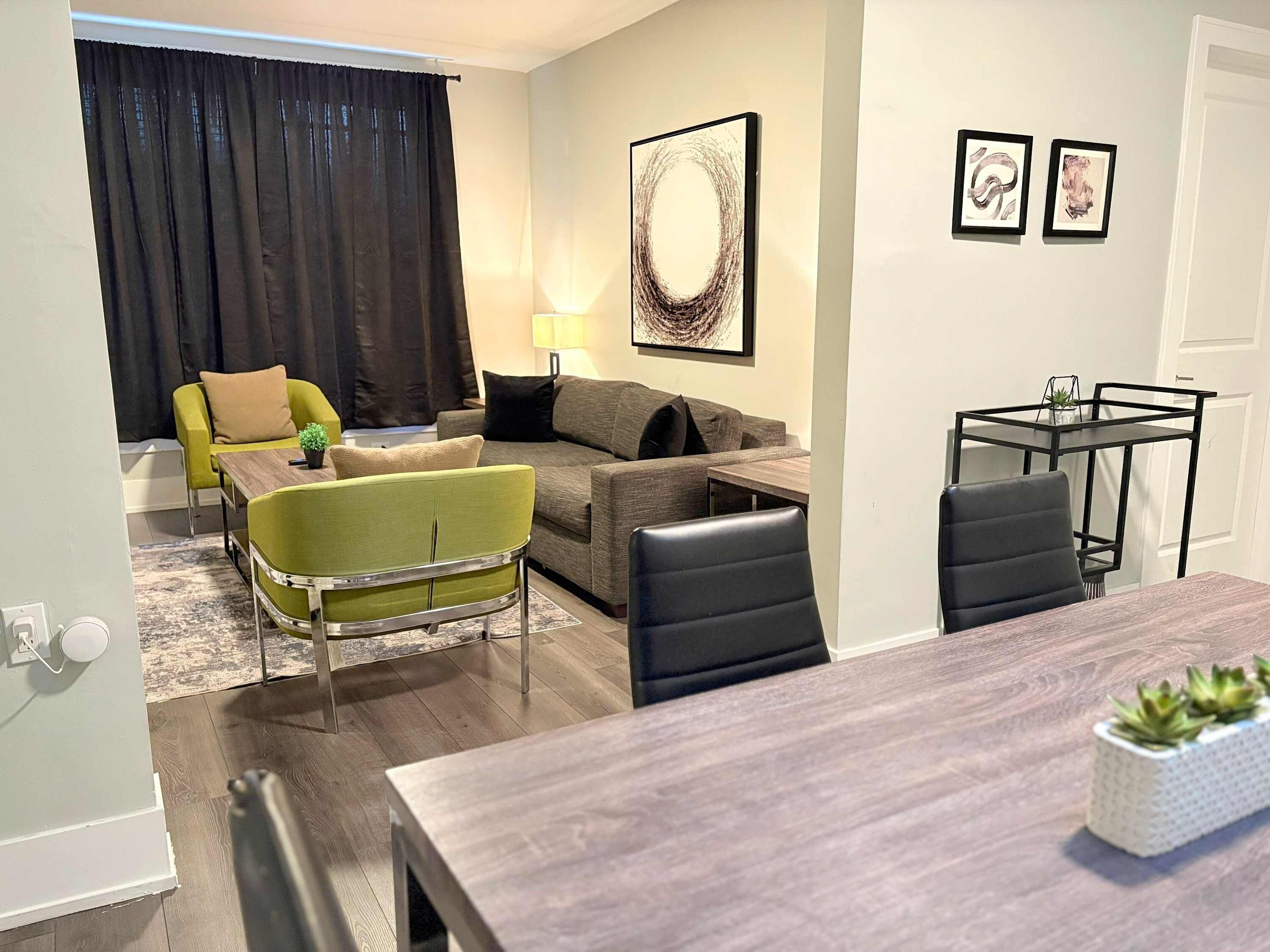 A modern living room with a sofa, a green armchair, a dining table, and a small side table with a plant.