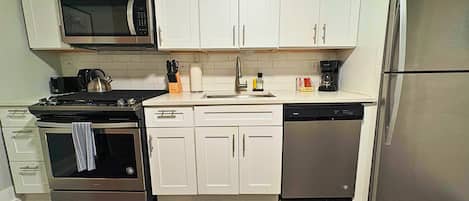 Une cuisine avec des meubles blancs, un réfrigérateur en acier inoxydable, un four à micro-ondes, une cuisinière et un lave-vaisselle.