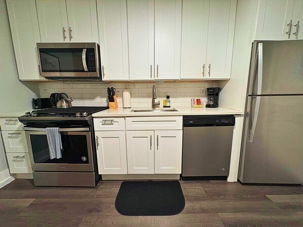 A kitchen with white cabinets, a stainless steel refrigerator, a microwave, a stove, and a dishwasher.