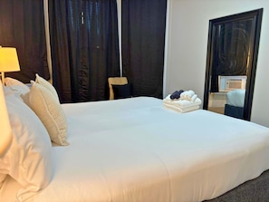 A neatly made bed with white linens, a stack of folded towels, and a mirror reflecting a part of the room.