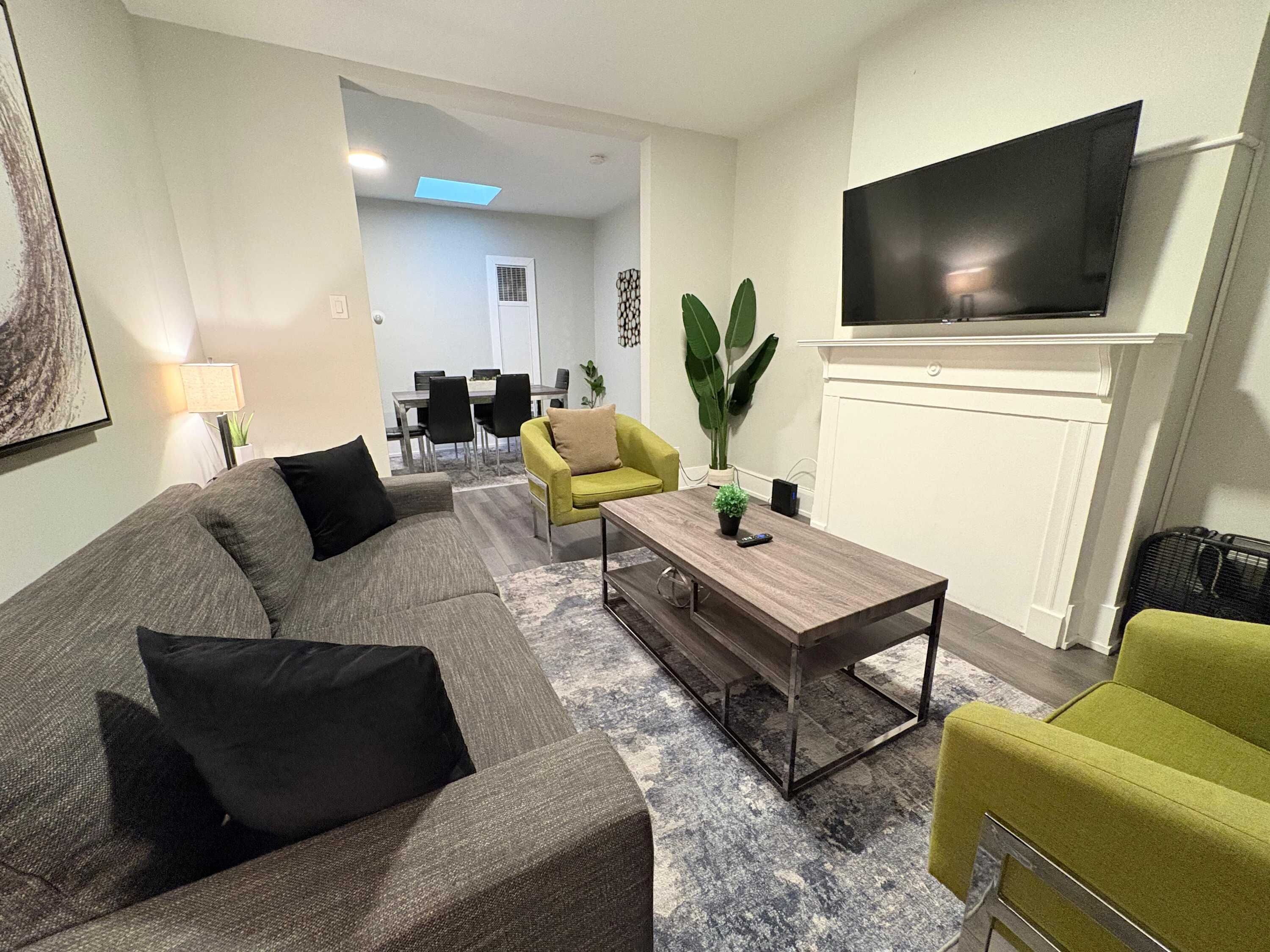 Una sala de estar moderna con un sofá gris, un sillón amarillo, una mesa de centro y un televisor de pantalla plana montado en la pared.
