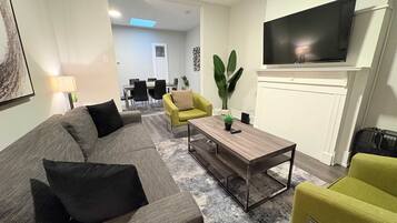 Una sala de estar moderna con un sofá gris, un sillón amarillo, una mesa de centro y un televisor de pantalla plana montado en la pared.