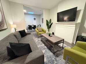 A modern living room with a grey sofa, a yellow armchair, a coffee table, and a flat-screen TV mounted on the wall. - Comfortably Appointed & Spacious 3BR Apartment (Chicago)