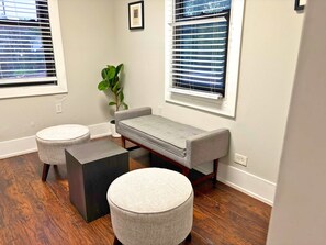 A room with a grey sofa, two round ottomans, a black side table, and a potted plant.