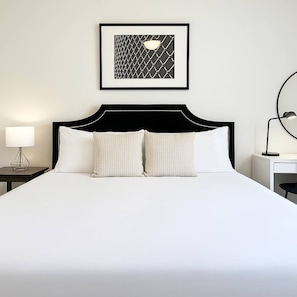 A neatly made bed with a black headboard and two pillows, a bedside table with a lamp, and a framed picture on the wall. - Ideal & Spacious 1BR Apt (Chicago)