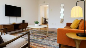 Ein modernes Wohnzimmer mit Flachbildfernseher, rundem Couchtisch, einer Couch und einem gemusterten Teppich.