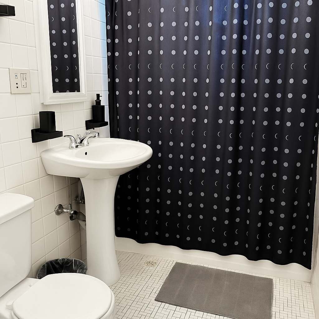 A bathroom with a white sink, a toilet, and a black curtain with white polka dots.