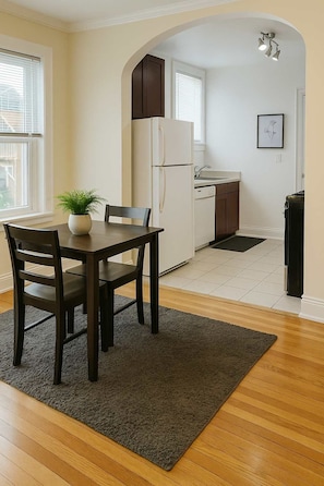 A compact kitchen with a refrigerator, sink, and cabinets. There is a dining table with chairs and a rug in the foreground. - Ideal & Spacious 1BR Apt (Chicago)