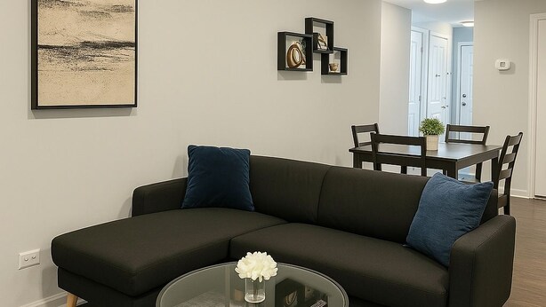 Een moderne woonkamer met een hoekbank, een glazen salontafel en een eethoek op de achtergrond.