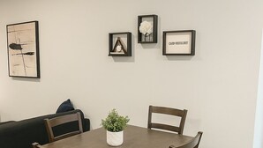 Een eetgedeelte met een houten tafel, vier stoelen, een potplant en kunstwerken in een lijst aan de muur.
