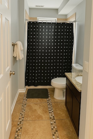 Un bagno con tenda doccia, water, lavandino e porta asciugamani.