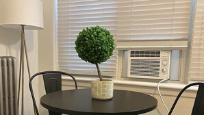 A round table with a potted plant, two black chairs, a floor lamp, and an air conditioning unit in a room with white walls and blinds. - 1BR Chic Apt in Downtown Chicago (Chicago)