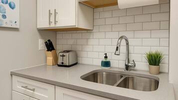 A kitchen with white cabinets, a stainless steel sink, a toaster, a soap dispenser, and a potted plant.