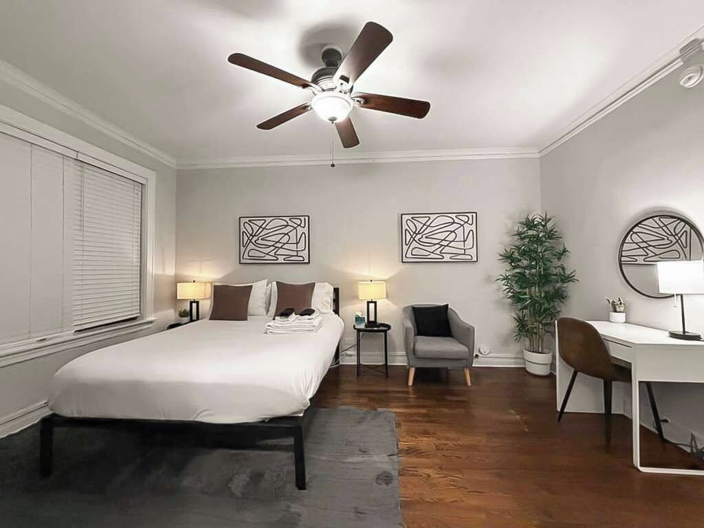 Habitación de hotel con cama, escritorio, silla, ventilador de techo y dos cuadros en la pared.