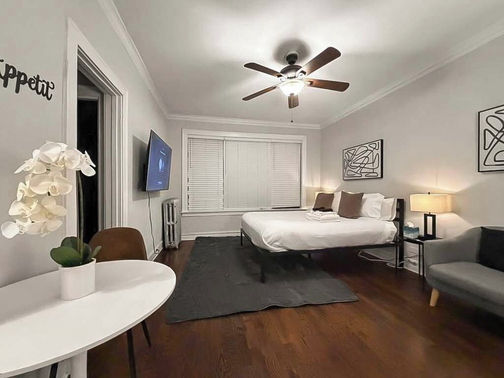 Habitación de hotel con cama, escritorio, silla, sofá, ventilador de techo, televisor y obras de arte en las paredes.