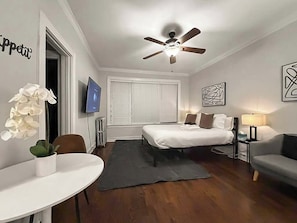 Habitación de hotel con cama, escritorio, silla, sofá, ventilador de techo, televisor y obras de arte en las paredes.