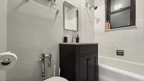 Een badkamer met een wit toilet, een zwart kastje, een spiegel en een raam.
