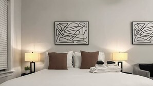 Een hotelkamer met een groot bed, twee abstracte kunstwerken aan de muur, twee bedlampen en een netjes opgevouwen stap handdoeken.