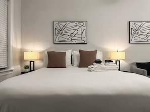 Ett hotellrum med en stor säng, två abstrakta konstverk som hänger på väggen, två sänglampor och en prydligt hopvikt hög med handdukar.