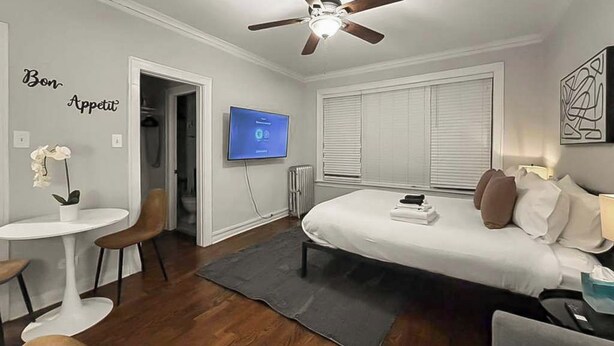Een moderne slaapkamer met een bed, een plafondventilator, een televisie en een klein tafeltje met stoelen.