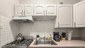 Een keuken met witte kastjes, een gasfornuis, een spoelbak en een koffiezetapparaat.