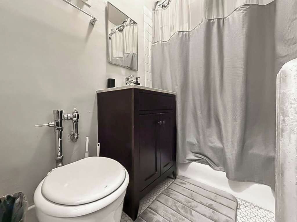 Un baño con inodoro, mueble de madera oscura y cortina de ducha.