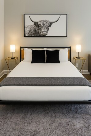 Habitació d'hotel amb un llit gran, dues làmpades de nit, una obra d'art emmarcada d'un bou i un sòl amb moqueta.