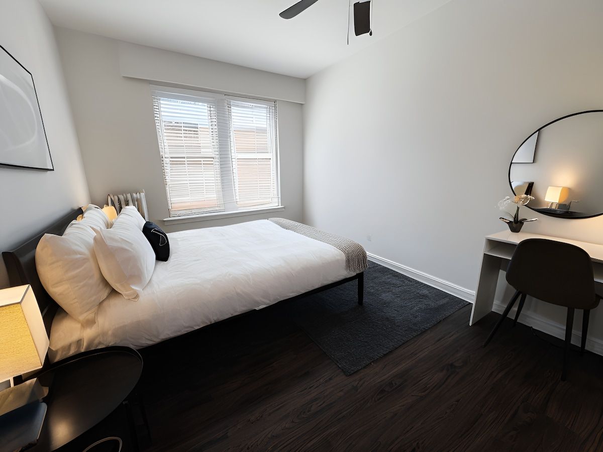 Une chambre à coucher avec un lit, un bureau, une chaise et une fenêtre avec des stores.
