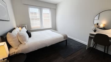 Quarto com cama, escrivaninha, cadeira e janela com persianas.