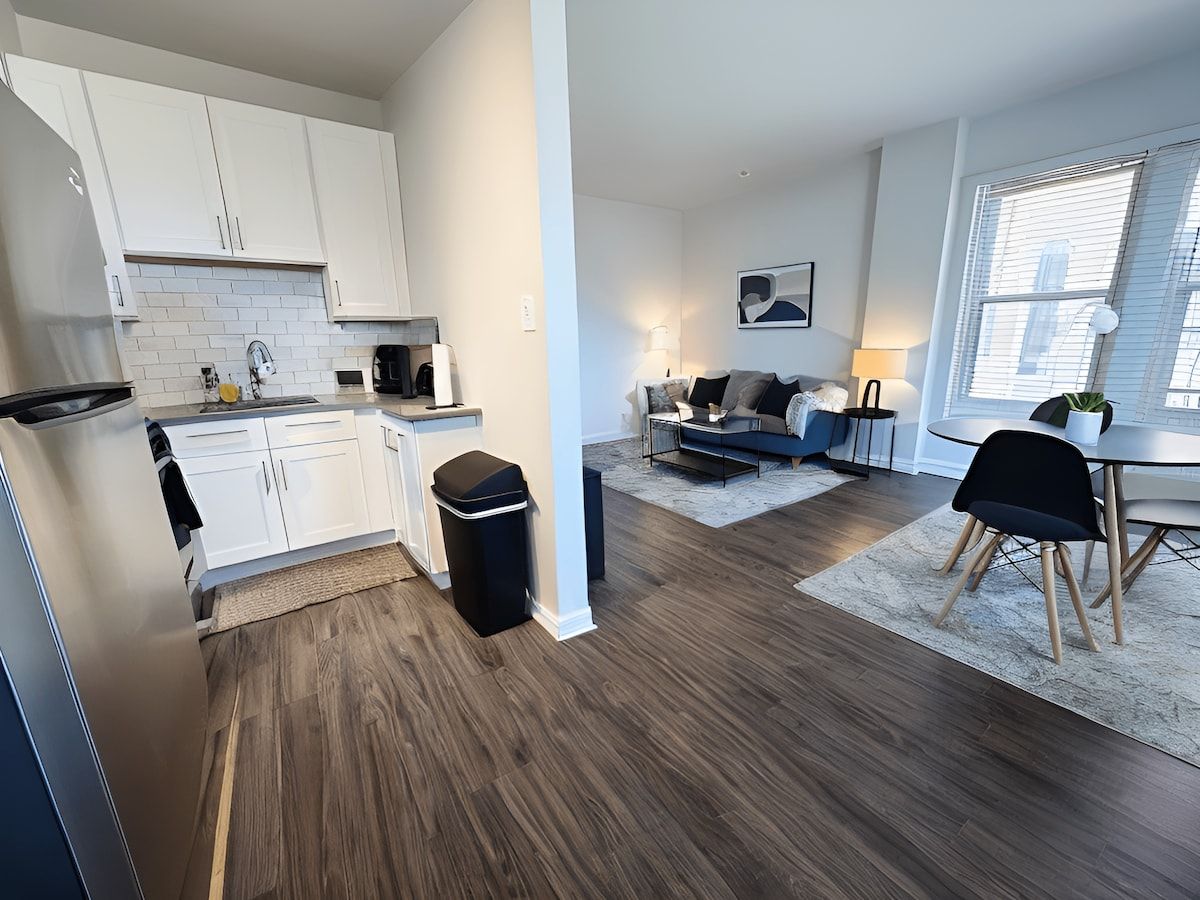 A modern kitchen with white cabinets, a black trash bin, and a dining area with a table and chairs.