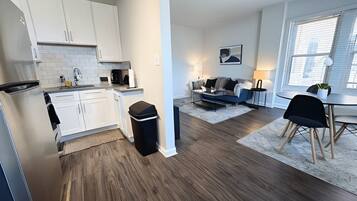 A modern kitchen with white cabinets, a black trash bin, and a dining area with a table and chairs.