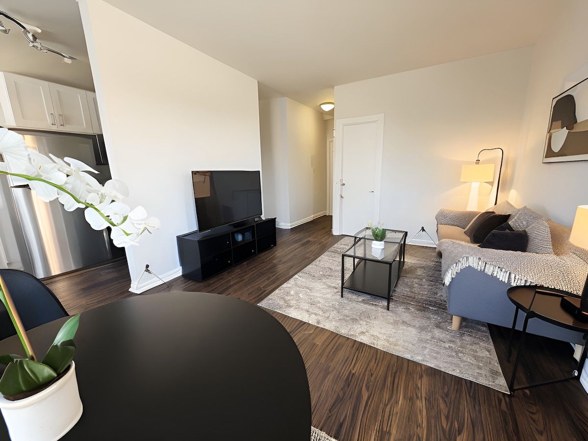 A modern living room with a flat-screen TV, a sofa, a coffee table, and a dining table.