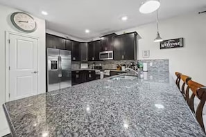 A kitchen with granite countertops, stainless steel appliances, and dark cabinetry. - 8BR Resort Home: Private Theater, Game Room, Heated Pool, Lazy River Near Disney (Four Corners)