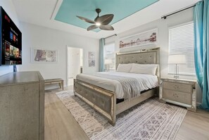 A modern bedroom with a bed, bedside tables, a ceiling fan, and a TV mounted on the wall. - 8BR Resort Home: Private Theater, Game Room, Heated Pool, Lazy River Near Disney (Four Corners)
