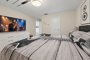 Un dormitori amb un llit que presenta un disseny de guitarra, una televisió a la paret i una porta.