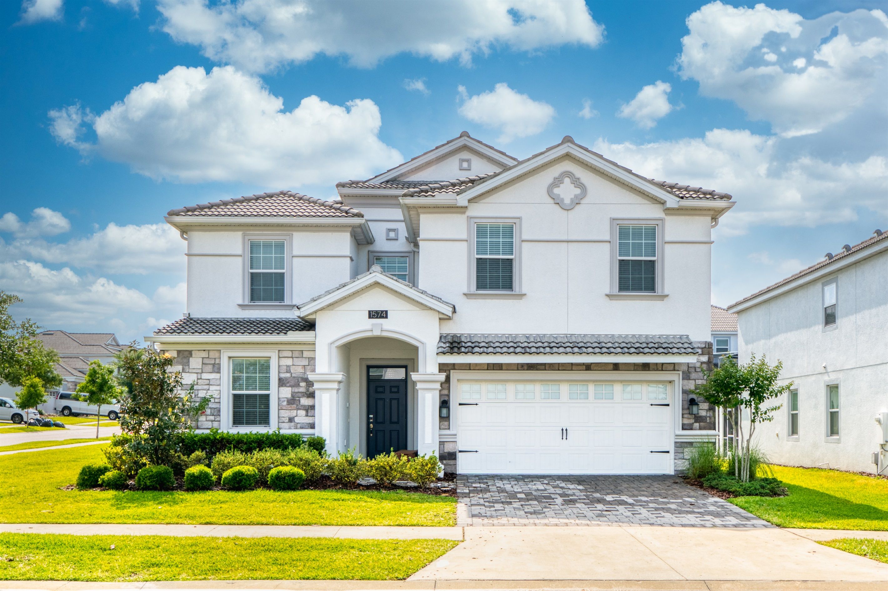 A two-story house with a garage, stone facade, and a well-maintained lawn.