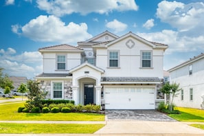 A two-story house with a garage, stone facade, and a well-maintained lawn. - 8BR Resort Home: Private Theater, Game Room, Heated Pool, Lazy River Near Disney (Four Corners)