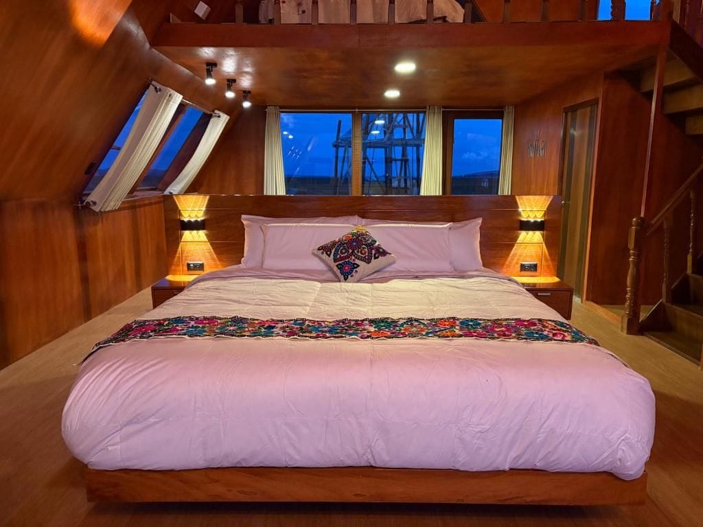 Une chambre avec un grand lit, des murs en bois, une lucarne et une vue sur l’extérieur.
