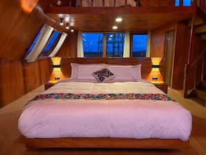 Un dormitorio con una cama grande, paredes de madera, un tragaluz y vistas al exterior.